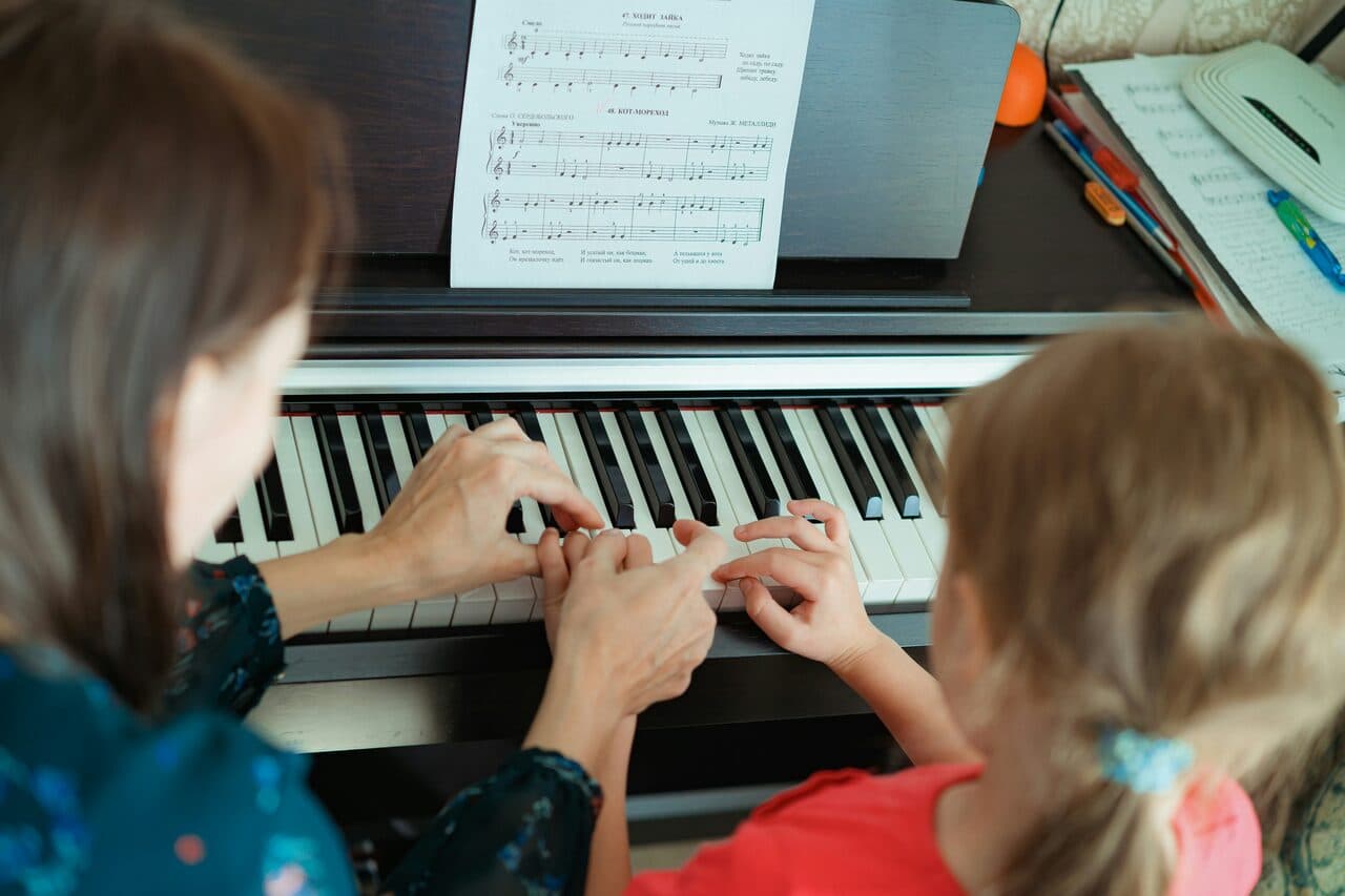 An adult teaching a child to play the piano during a lesson